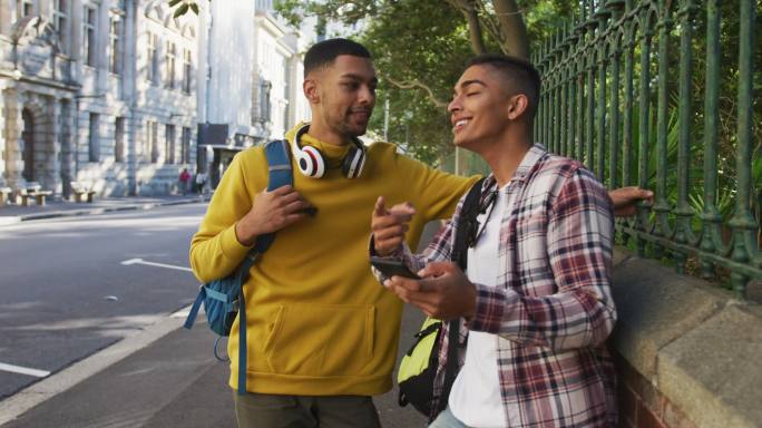 两个快乐的混血男性朋友站在街上使用智能手机