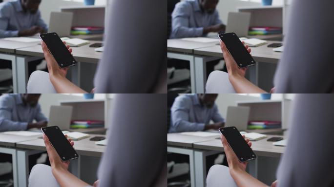 混血女商人坐在办公桌前，在办公室使用智能手机，屏幕上有打印空间