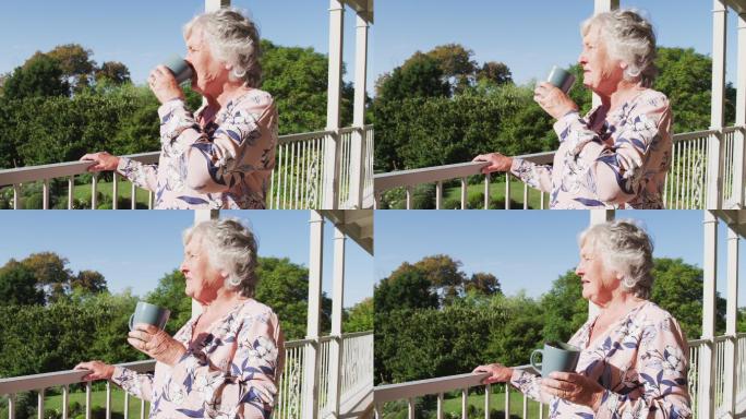 一位深思熟虑的白人老年妇女站在家里的阳台上喝咖啡