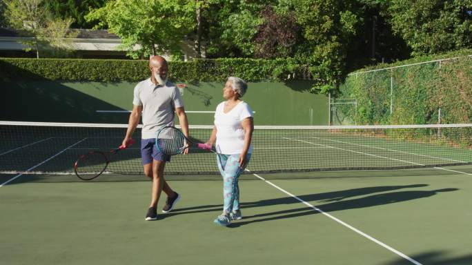 非裔美国老年夫妇拿着球拍在网球场上交谈