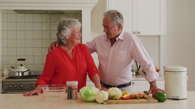 白人老年夫妇在家里的厨房里互相拥抱的画像