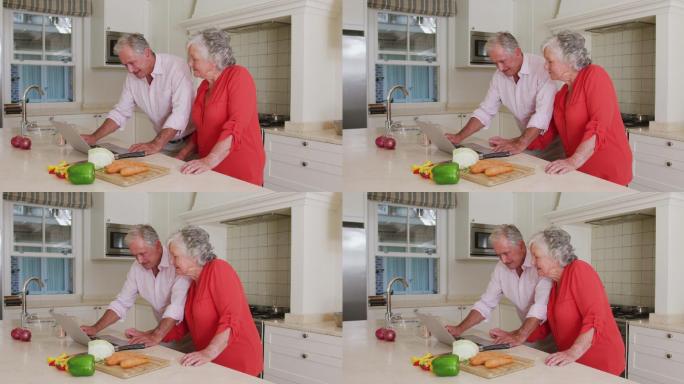 快乐的白种人老夫妇在厨房使用笔记本电脑的食谱准备饭前
