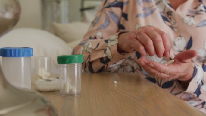 中年白人老年妇女在家里从药用容器中取出药丸