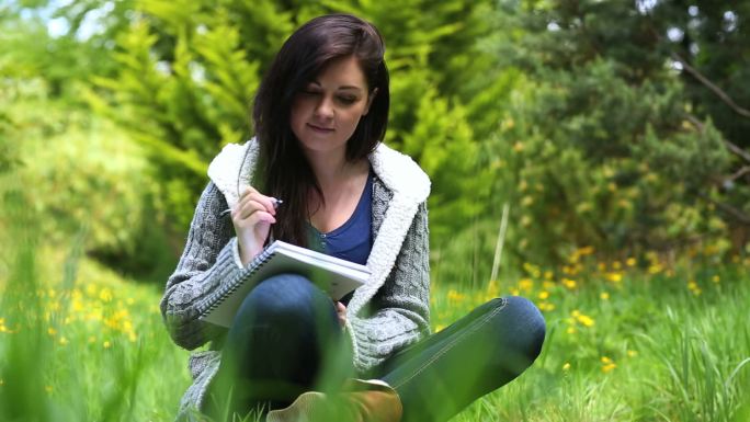 漂亮女人坐在草地上在笔记本上写字