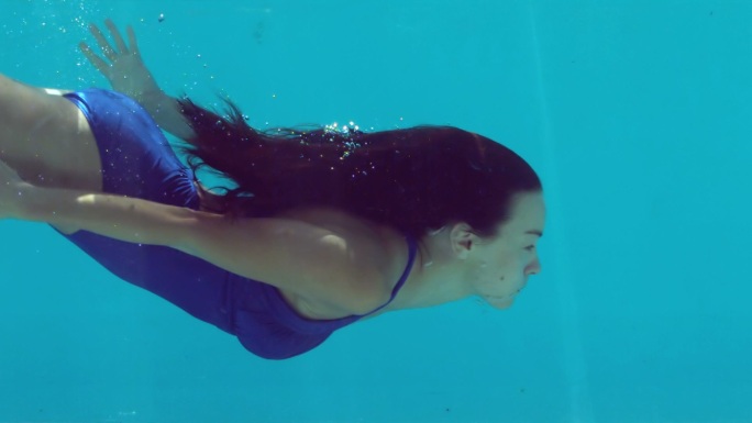 深色头发的女人在水下游泳在蓝色泳衣在慢动作