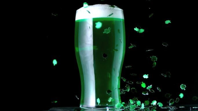 三叶草碎片飘落在一杯绿色啤酒旁边特写