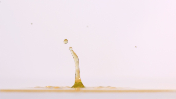绿色液滴在黄色液体中以超慢的运动下落，背景是白色