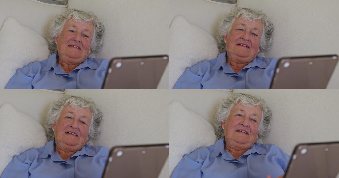 白种老年女性躺在家里的沙发上使用电子平板电脑