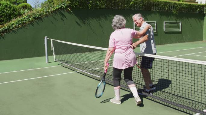快乐的白人老年夫妇在打完一场比赛后拥抱在室外网球场的网
