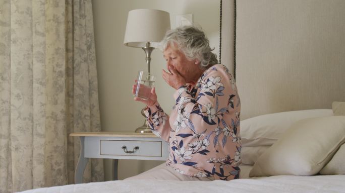 中年白人老年妇女坐在家里的床上服用药物