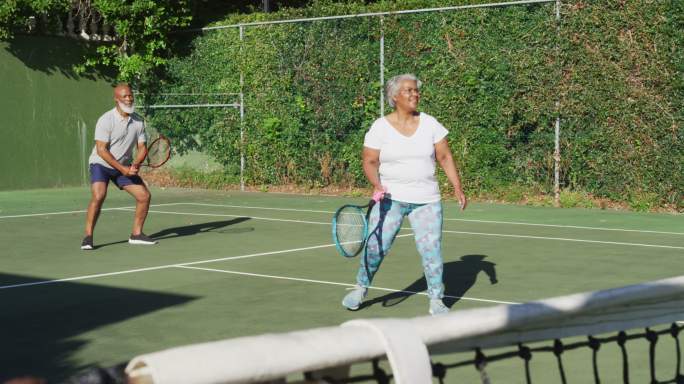 一对非裔美国老年夫妇在一个阳光明媚的日子里在网球场上打网球