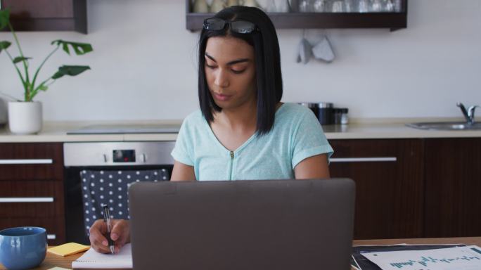 不同种族、不同性别的人坐在办公桌前做笔记，在家用笔记本电脑工作