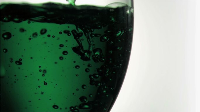 在白色的背景下，绿色的涓涓细流以超慢的动作倒满一杯酒