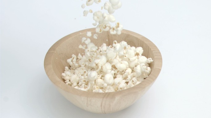 在白色的背景下，爆米花以超慢镜头落在一个木碗里