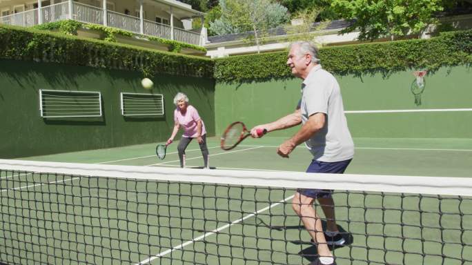 快乐的白种人老年夫妇在户外网球场打比赛后，作为双打队