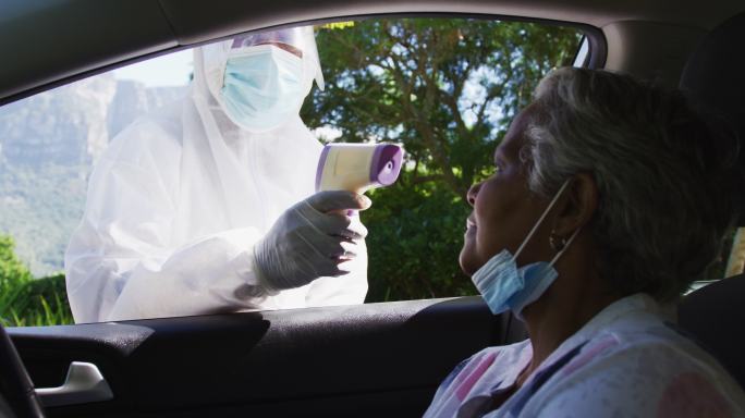 穿着防护服的卫生工作者在车内测量非裔美国老年妇女的体温