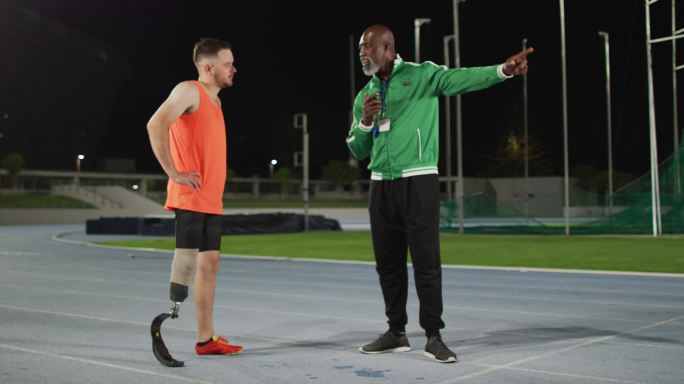 多样化的男教练和残疾男运动员与跑步刀片站立和说话