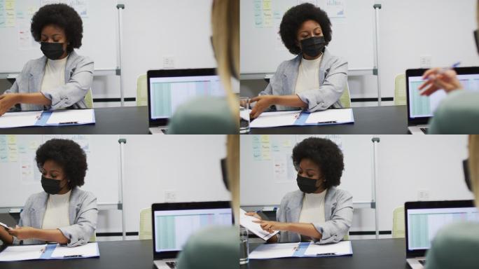 非裔美国女商人戴着口罩拿着文件与办公室的同事交谈