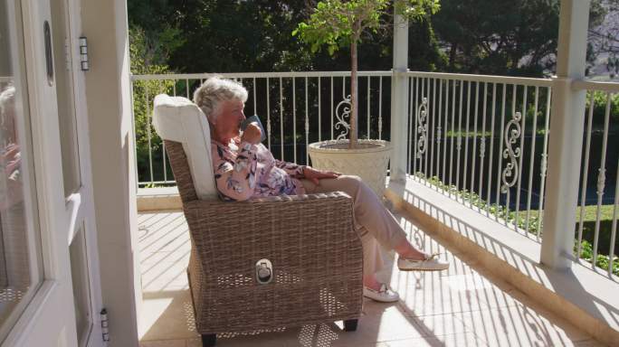 坐在家里阳台的椅子上喝咖啡的白人老年女性