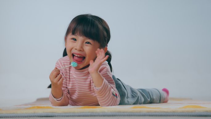 快乐的小女孩趴在地毯上吃棒棒糖