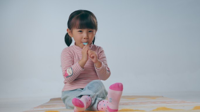 快乐的小女孩坐在地毯上吃棒棒糖