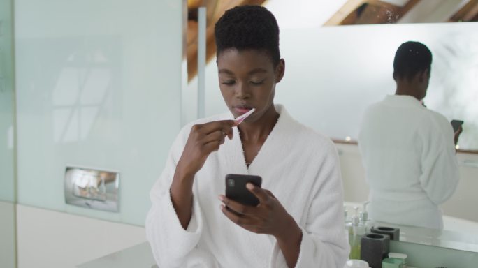 非洲裔美国美女在浴室刷牙和使用智能手机
