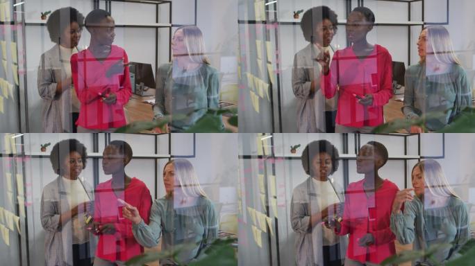 3名不同类型的女商人在办公室的玻璃墙上写下备忘录，进行头脑风暴