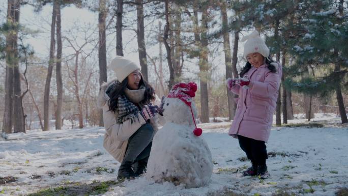 年轻妈妈和女儿在雪地里堆雪人