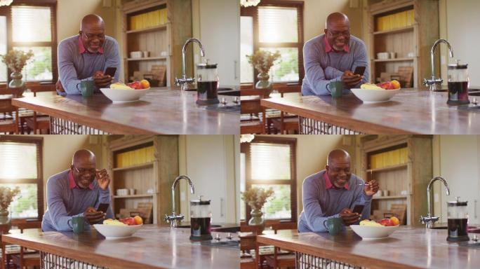 非裔美国老人靠在厨房柜台上用智能手机，摘掉眼镜，微笑着