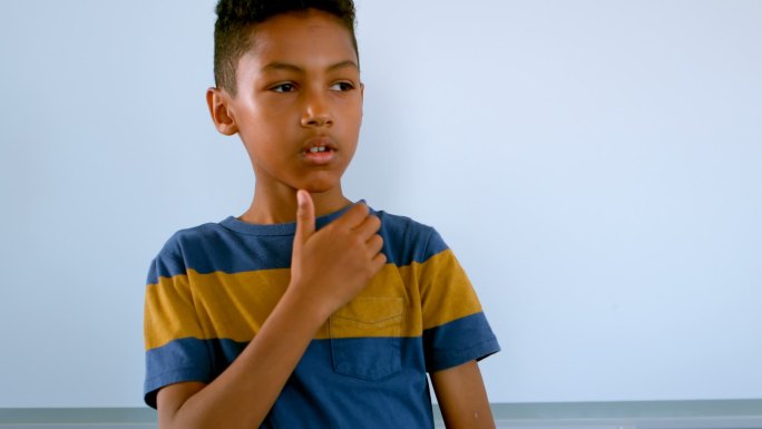 一个非洲裔美国男孩，手托着下巴，靠着白板站在4k教室里