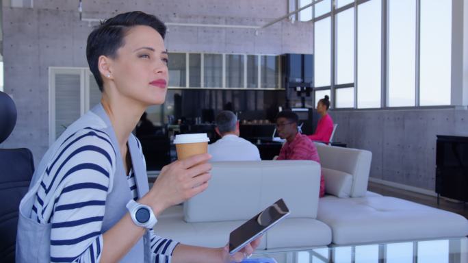 美丽的白人女商人使用数字平板电脑，同时在现代办公室喝咖啡4k