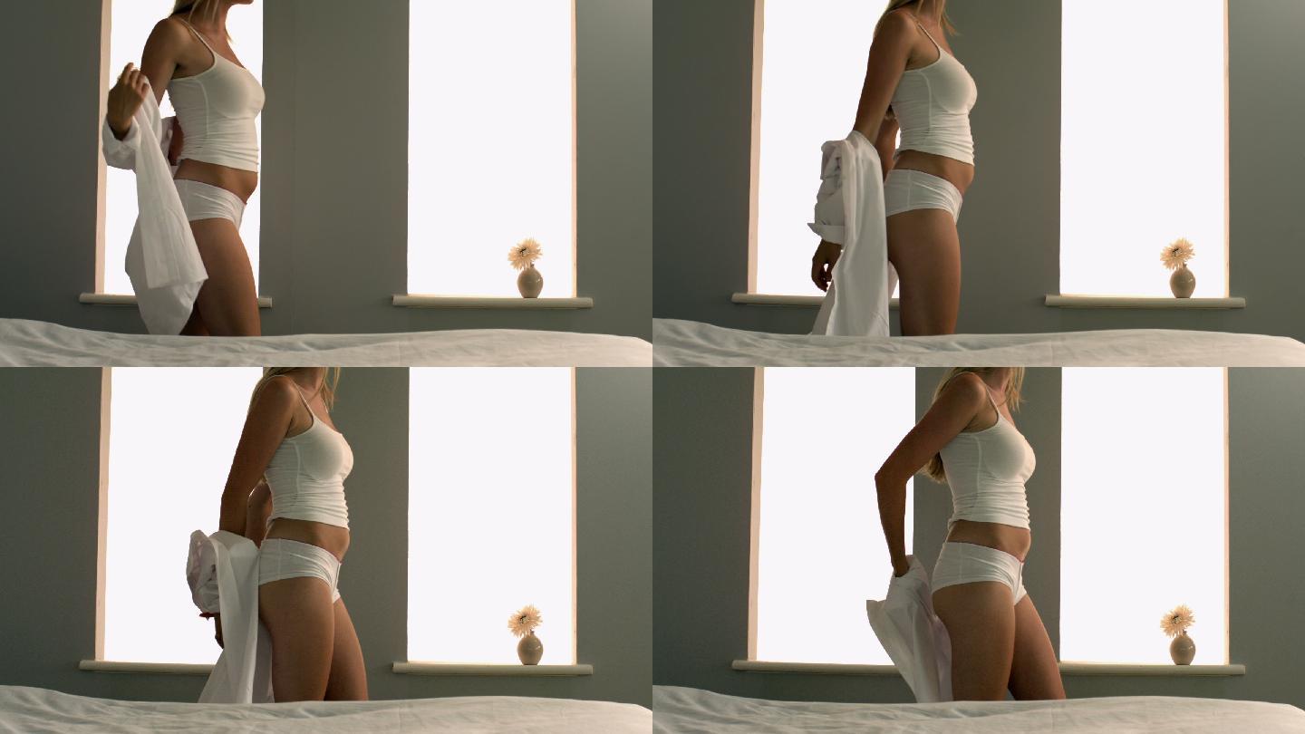 在明亮的卧室里，迷人的金发女郎正在慢镜头中脱光衣服