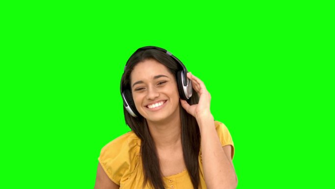 女人在绿色背景下戴着耳机听音乐特写