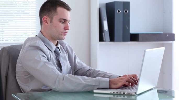 一个穿着考究的男人在办公室里用笔记本电脑打字