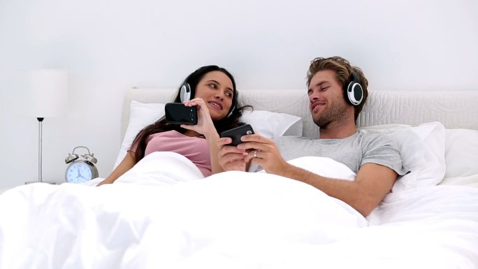 一对夫妇躺着床上戴着耳机听歌特写