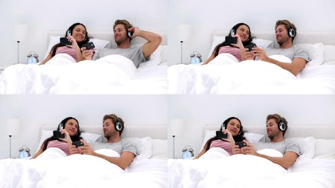 一对夫妇躺着床上戴着耳机听歌特写