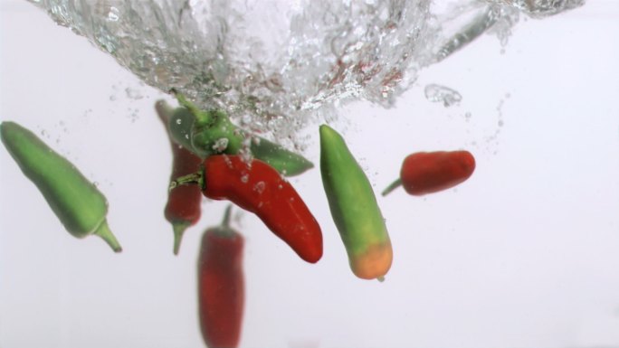 红色和绿色辣椒水中落下慢镜头，在白色背景下