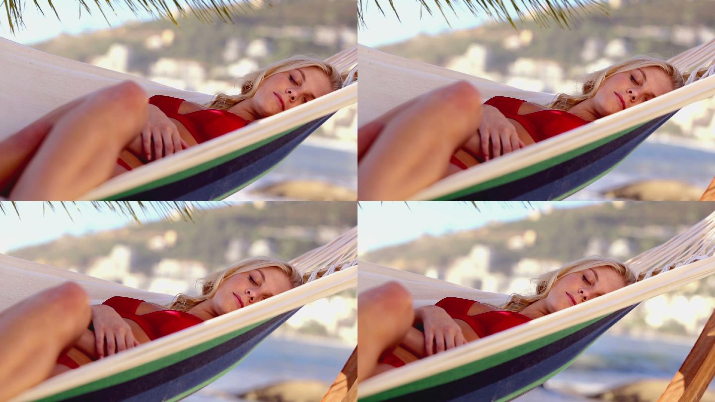 迷人的金发女人睡在沙滩上的吊床上