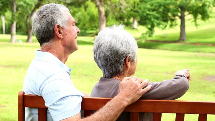 一对退休夫妇在一个阳光明媚的日子里一起坐在公园的长椅上