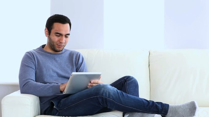 一个坐在沙发上用着平板电脑的快乐男人