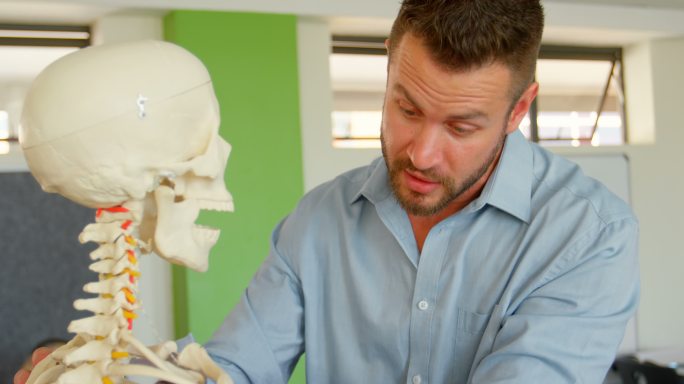 白人男老师带着人体骨骼模型在学校教室里4k