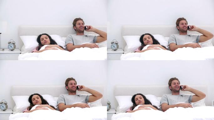 一个男人在打电话，而他的伴侣在家里的床上睡觉