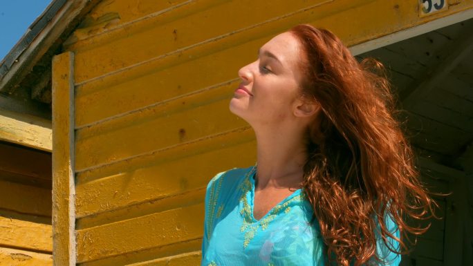 美丽的年轻白人女人站在海滩小屋在4k的阳光下