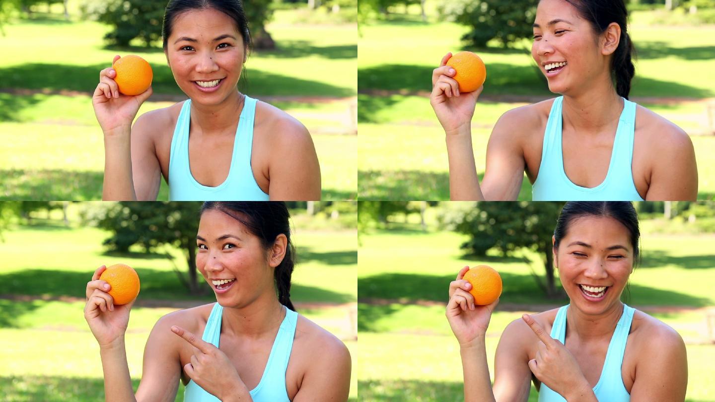 健康的亚洲女孩在一个阳光明媚的日子展示一个桔子