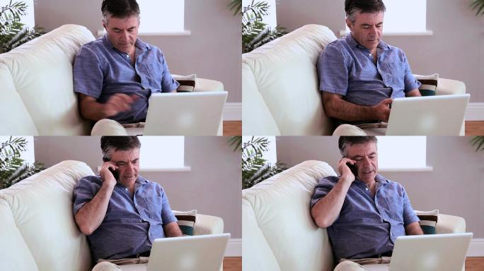 一个成熟的男人坐在沙发上，在客厅里用笔记本电脑接电话