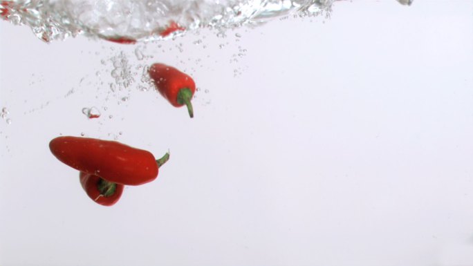 辣椒在白色背景下以超慢的动作落到水中