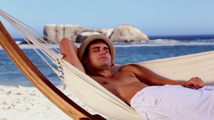 一个戴着草帽的男人躺在沙滩上的吊床上休息