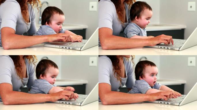 母亲和婴儿坐在膝盖上，在厨房里使用笔记本电脑