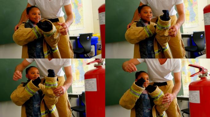 男消防员帮助非裔美国女孩在教室穿消防制服。女孩微笑