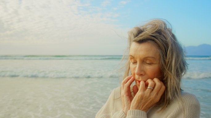 活跃的白人老女人闭着眼睛站在沙滩上4k